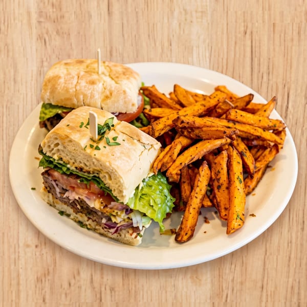 Two sandwiches with meat, lettuce, and tomato, served with a side of sweet potato fries.