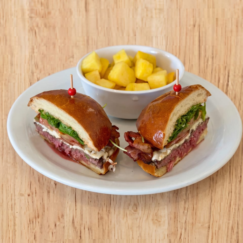 Two halves of a gourmet burger with bacon, lettuce, and sauce, served with a side of cubed potatoes.